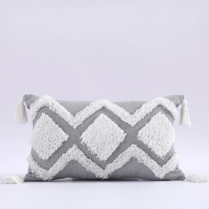 Gray and white pillow with geometric pattern and tassels on a light gray background