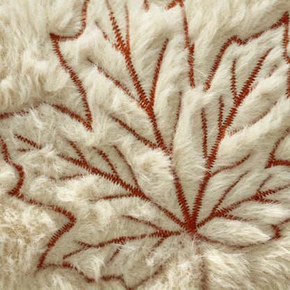 Close-up of a textured cream faux fur surface with a raised rust-orange leaf pattern stitched or embroidered into it.