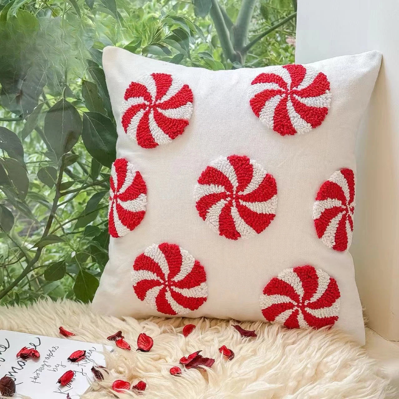 Decorative pillow with red and white peppermint pattern on a fluffy surface with greenery in the background.