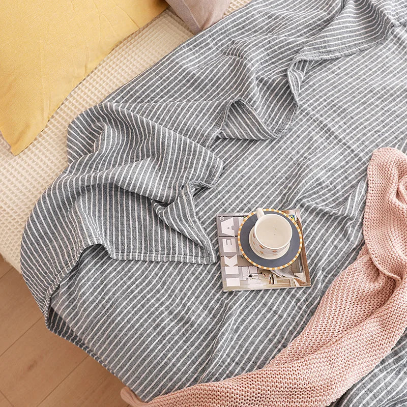 Gray striped blanket draped over a surface with a small decorative item on top. Boho Lightweight microfiber summer blanket for bed or sofa, cooling breathable throw for home, dorm, or office naps with geometric jacquard pattern.