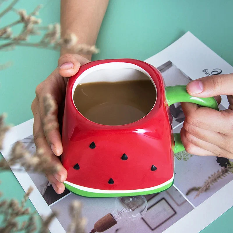 Red watermelon-shaped mug with green handle held by hands on a magazine background Creative watermelon ceramic mug, kawaii coffee and milk cup with hand-painted design, 500ml porcelain drinkware for kitchen decor