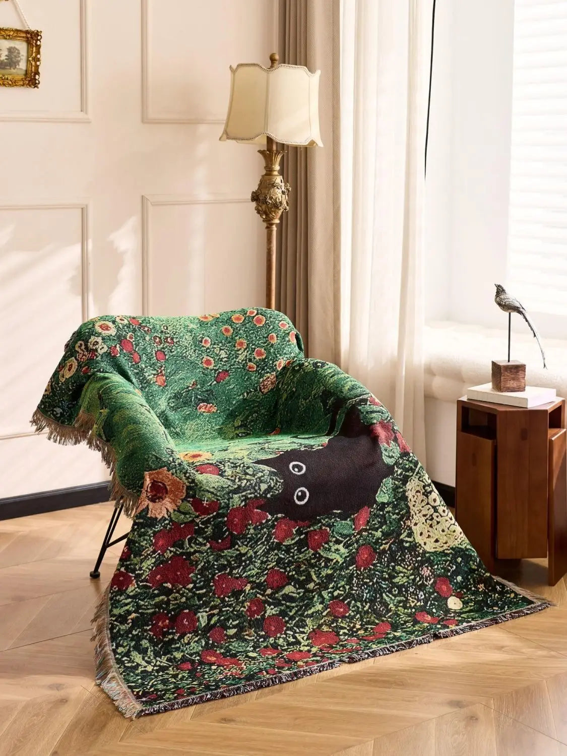 Green floral-patterned blanket draped over a chair in a room with a lamp and window. Cat woven throw blanket for boho sofa and home decor