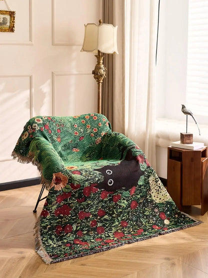 Green floral-patterned blanket draped over a chair in a room with a lamp and window. Cat woven throw blanket for boho sofa and home decor
