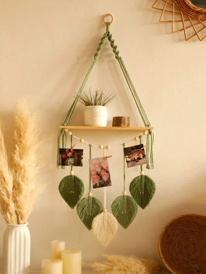 Hanging plant holder with wooden shelf, plants, and decorative elements against a beige wall.