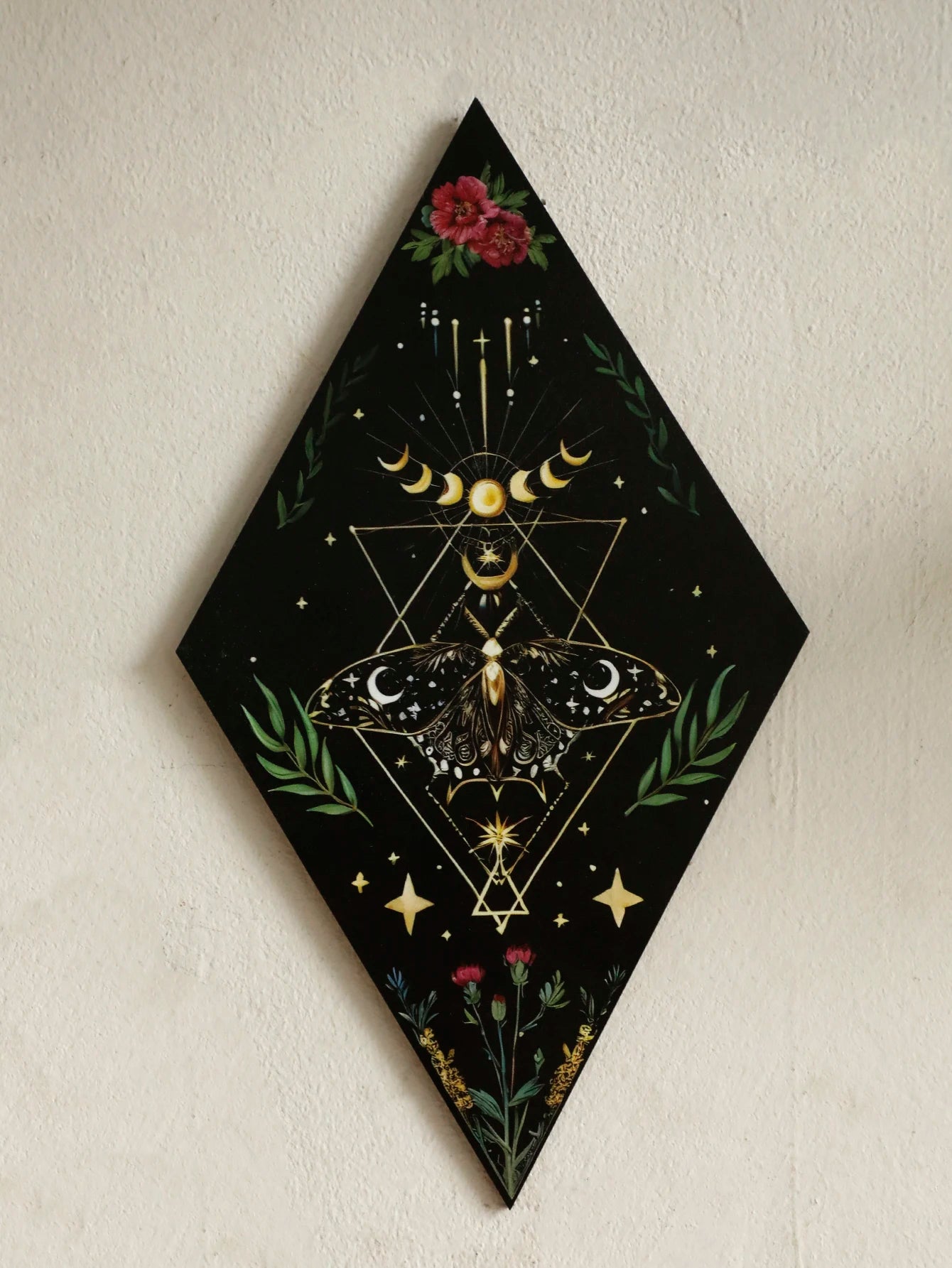Decorative wall art with moth, moon phases, and floral elements on a black background. Rustic colorful wood wall art panel with moon, stars, and butterfly engraving, displayed above a sofa in a boho-styled living room