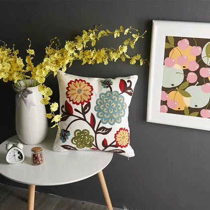 Decorative pillow with floral pattern on a small round table against a dark wall with a framed picture. Handcrafted embroidered cushion cover on armchair – modern boho living room decor