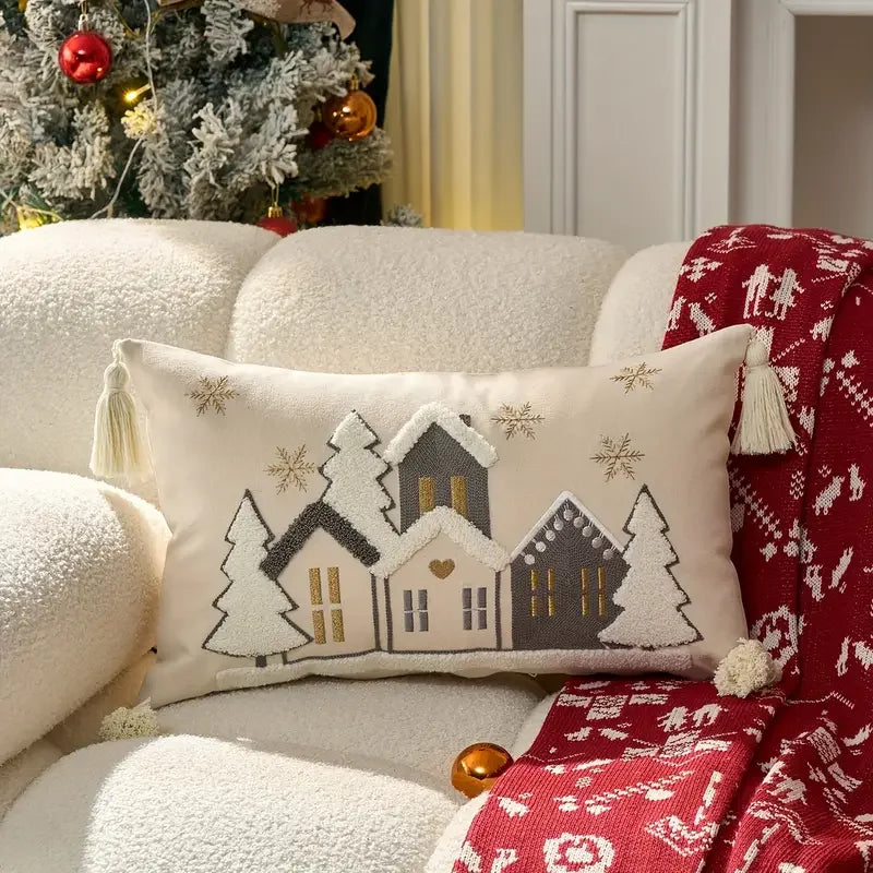 Decorative pillow with winter scene design on a white couch with a red blanket.