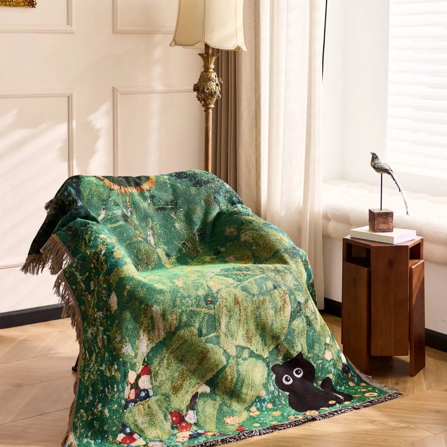 Green patterned blanket draped over a chair in a room with a lamp and small table. Cat woven throw blanket for boho sofa and home decor