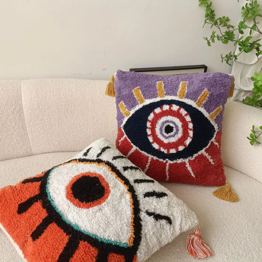 Two decorative pillows with eye designs on a couch. Boho Devil's Eye embroidered pillow cover with tufted geometric design in cotton blend fabric, decorative cushion for sofa, bed, or living room boho home decor.