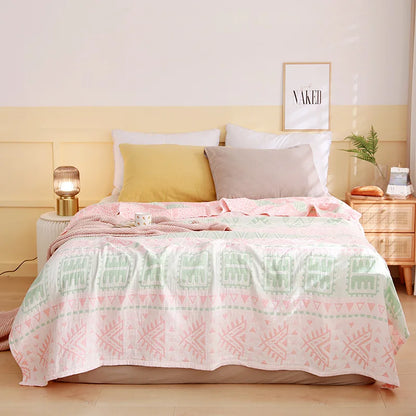 Bedroom with a bed featuring a pink and green patterned comforter, white pillows, and a nightstand with a lamp. Boho Lightweight microfiber summer blanket for bed or sofa, cooling breathable throw for home, dorm, or office naps with geometric jacquard pattern.