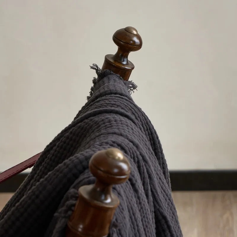 Gray scarf draped over a wooden coat rack against a neutral background Maillard cotton gauze blanket with tassels, four-layer muslin throw for sofa, bed, and boho home decor