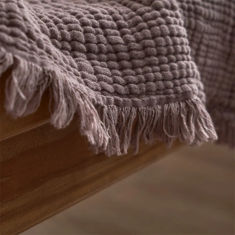 Textured blanket with tassels draped over a wooden surface Maillard cotton gauze blanket with tassels, four-layer muslin throw for sofa, bed, and boho home decor