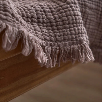 Textured blanket with tassels draped over a wooden surface Maillard cotton gauze blanket with tassels, four-layer muslin throw for sofa, bed, and boho home decor