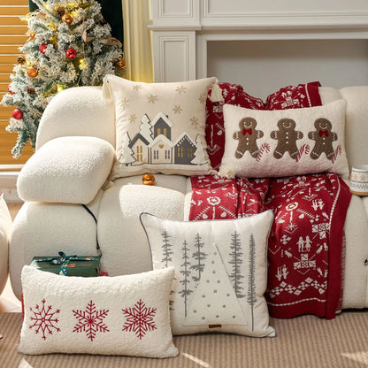Decorative pillows with gingerbread men, snowflakes and snowy village, and blanket on a couch with a Christmas tree in the background