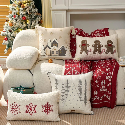 Decorative pillows with gingerbread men, snowflakes and snowy village, and blanket on a couch with a Christmas tree in the background