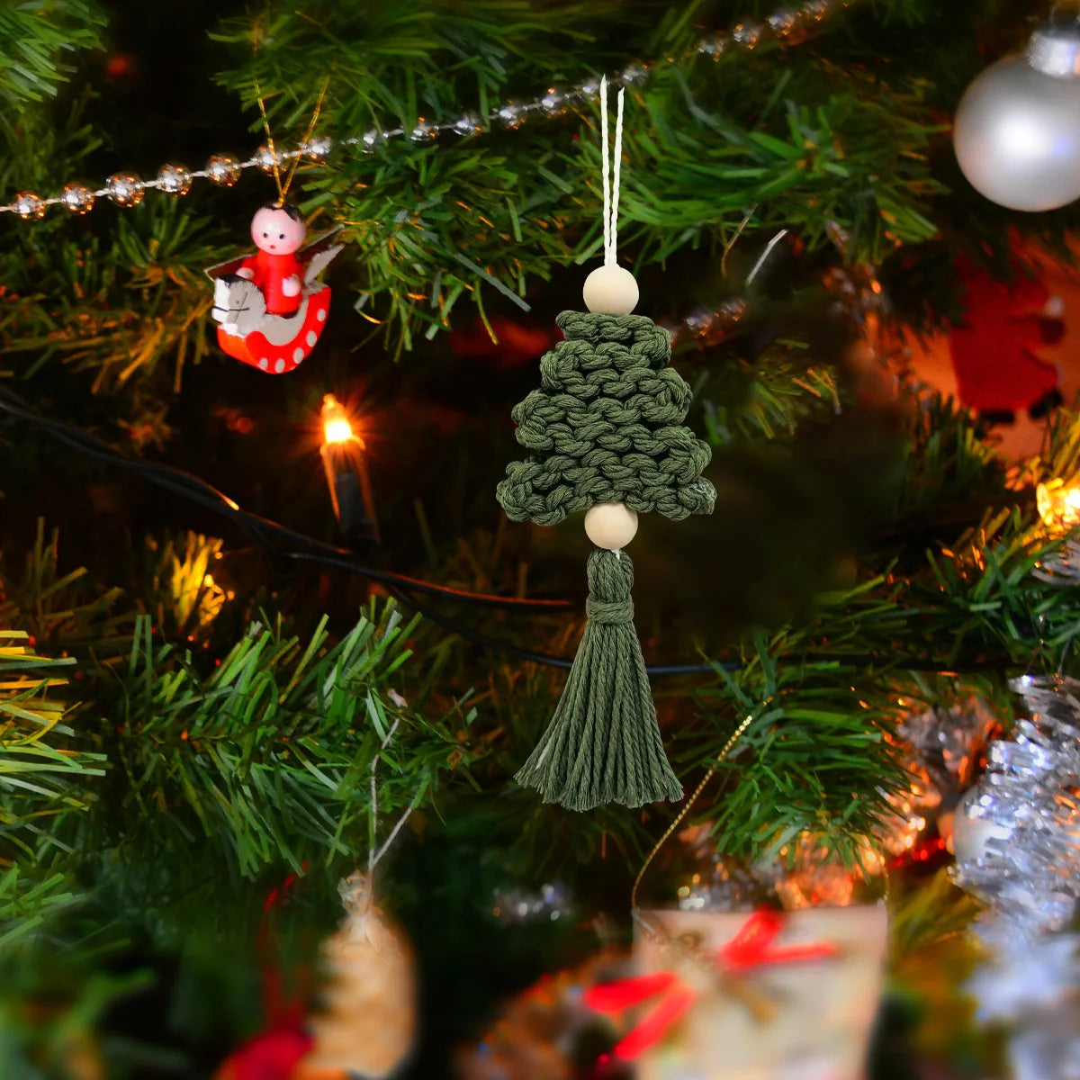Green knitted Christmas tree ornament with tassel hanging on a decorated tree.