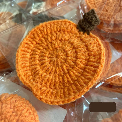 Orange crocheted item on a clear plastic background. Handmade crochet pumpkin coaster in cotton, Halloween table decor for mugs and drinks, festive DIY autumn party accessory