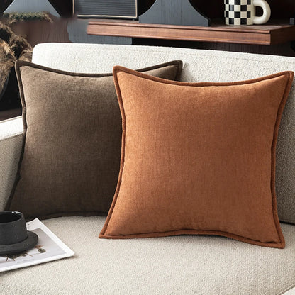 Two brown pillows on a beige sofa with a coffee table and decorative items in the background.