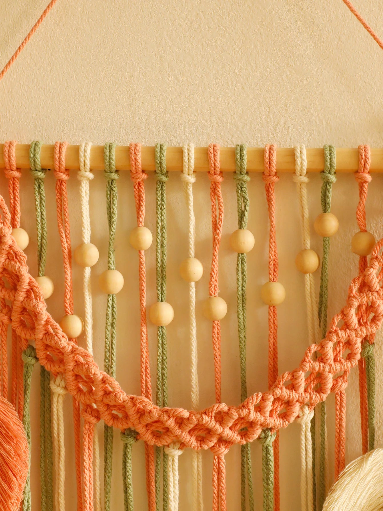 Macrame wall hanging with peach and green ropes on a beige background