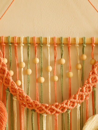 Macrame wall hanging with peach and green ropes on a beige background