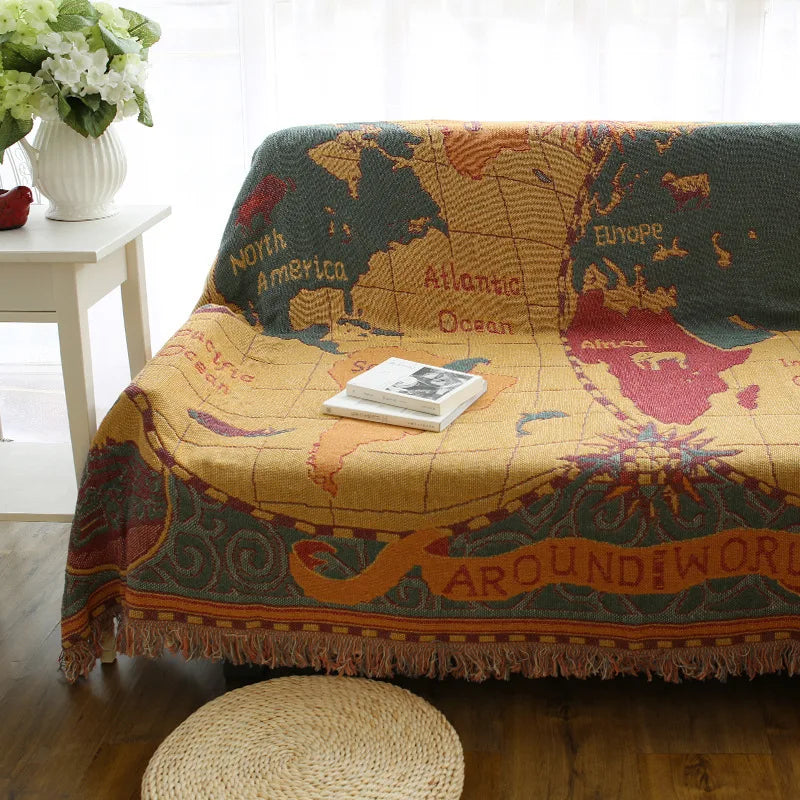 Map-themed blanket draped over a couch with a small stool and flowers in the background. Travel-inspired cotton plaid bed cover and decorative boho blanket