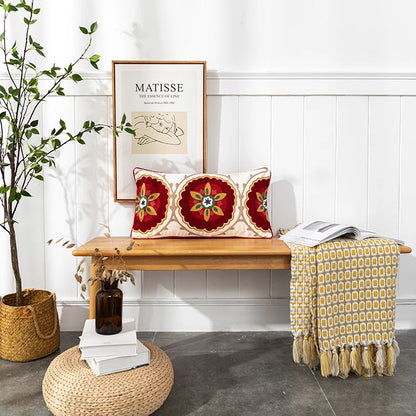 Decorative pillows on a wooden bench with a plant and books in the background. Bohemian embroidered throw pillow cover with geometric design, cotton-blend cushion for sofa, bed, or modern home decor.