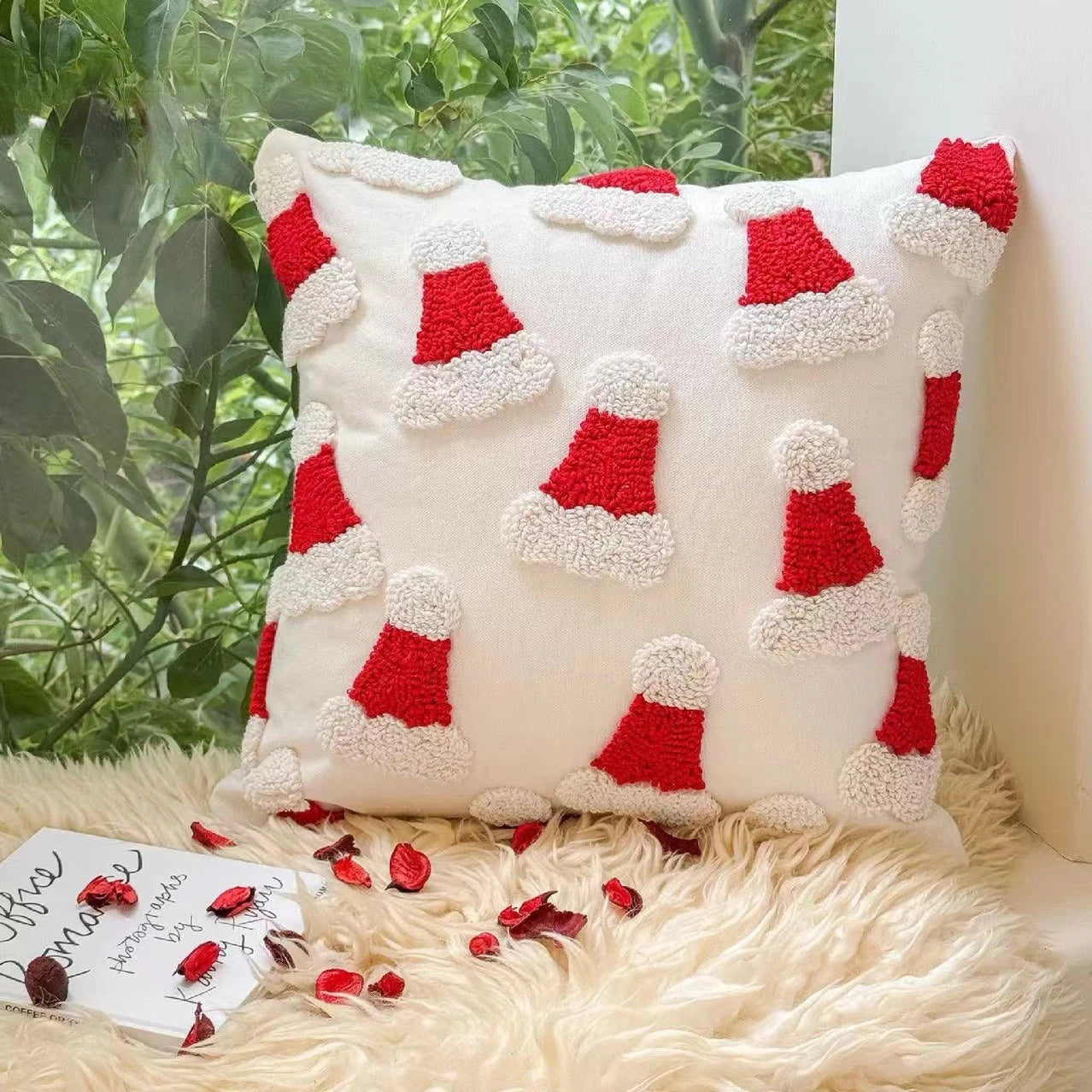 Decorative pillow with red and white Santa hats pattern on a fluffy surface with plants in the background