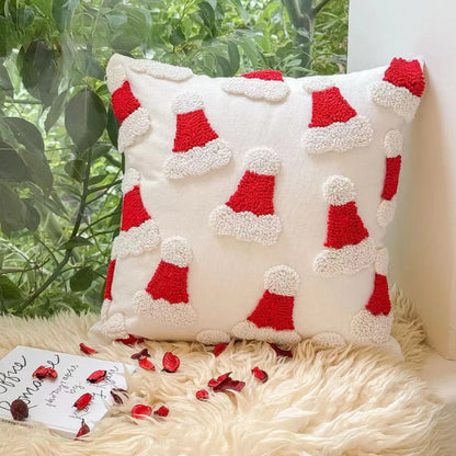 Decorative pillow with red and white Santa hats pattern on a fluffy surface with plants in the background