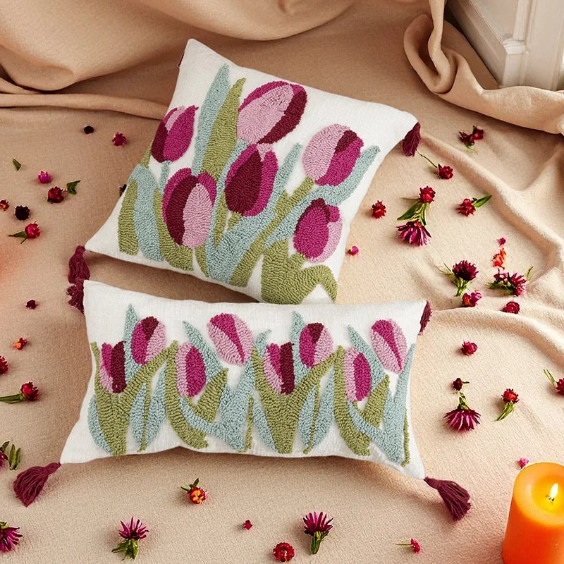 Two embroidered tulip-patterned pillows on a beige fabric background with scattered flower petals.