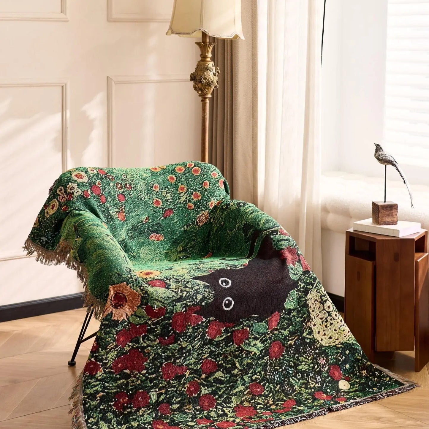 Decorative green floral blanket draped over a chair in a room with a lamp and side table. Cat woven throw blanket for boho sofa and home decor
