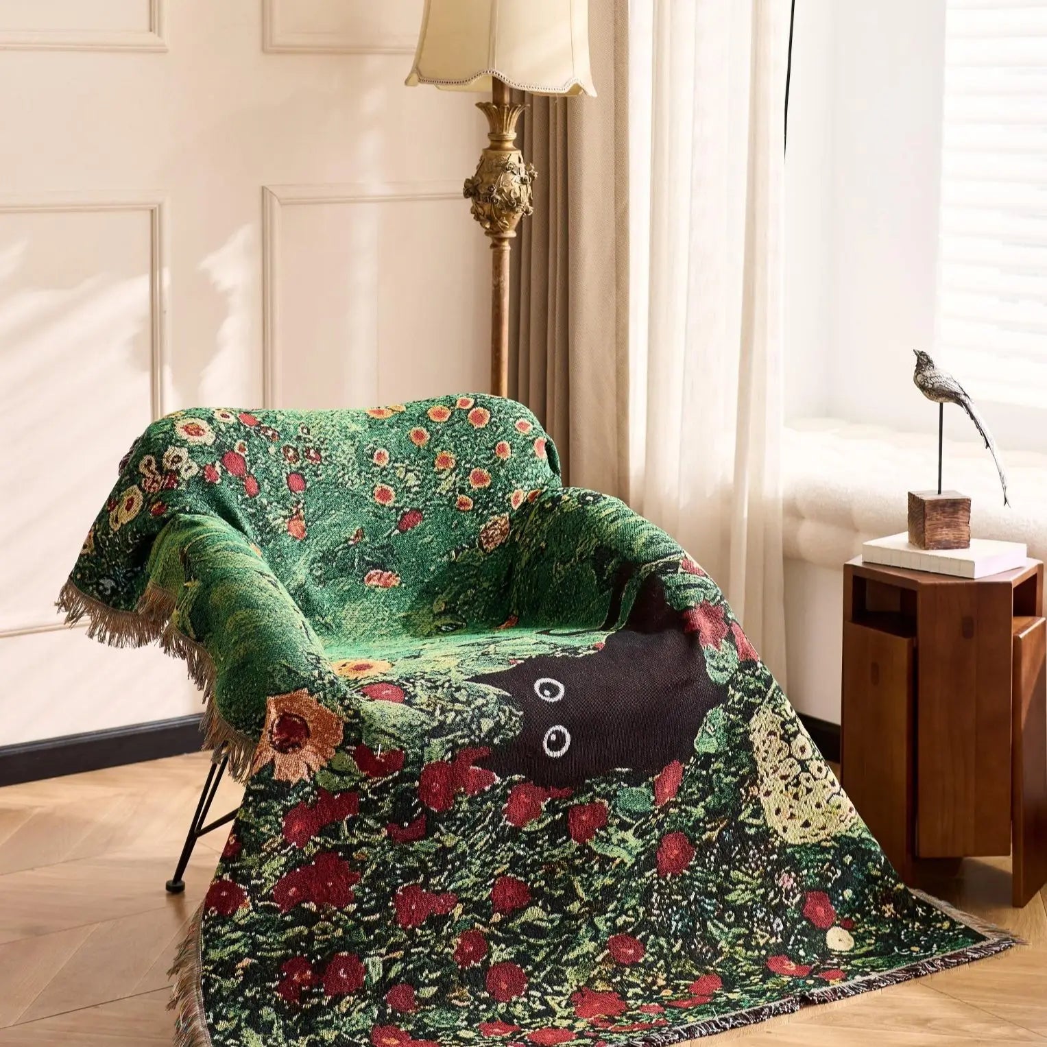 Decorative green floral blanket draped over a chair in a room with a lamp and side table. Cat woven throw blanket for boho sofa and home decor