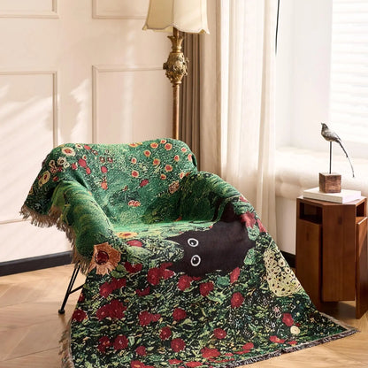 Decorative green floral blanket draped over a chair in a room with a lamp and side table. Cat woven throw blanket for boho sofa and home decor