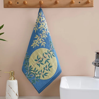 Blue tea towel with green leaf pattern hanging on a wooden towel rack above a sink.