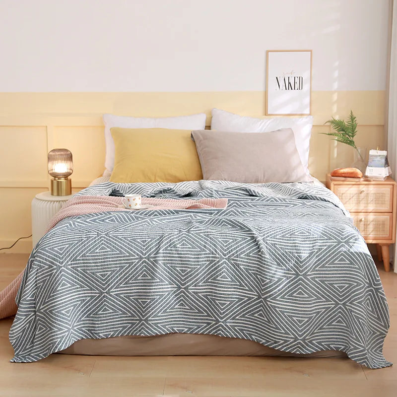 Bedroom with a bed featuring a geometric patterned comforter, pillows, and nightstands. Boho Lightweight microfiber summer blanket for bed or sofa, cooling breathable throw for home, dorm, or office naps with geometric jacquard pattern.