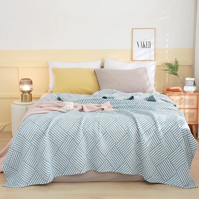 Bed with a geometric patterned quilt, pillows, and a lamp in a bedroom setting. Boho Lightweight microfiber summer blanket for bed or sofa, cooling breathable throw for home, dorm, or office naps with geometric jacquard pattern.