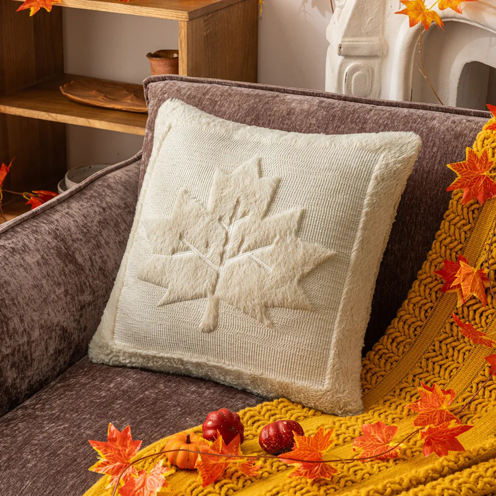 Decorative pillow with a leaf pattern on a couch surrounded by autumn leaves and decorations. Halloween pumpkin plush pillow cover for sofa and bed decor.
