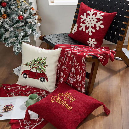 Decorative pillows with Christmas designs on a chair next to a tree. Embroidered Merry Christmas pillow cover with snowflake design – festive red and white holiday cushion for sofa or bedroom décor.