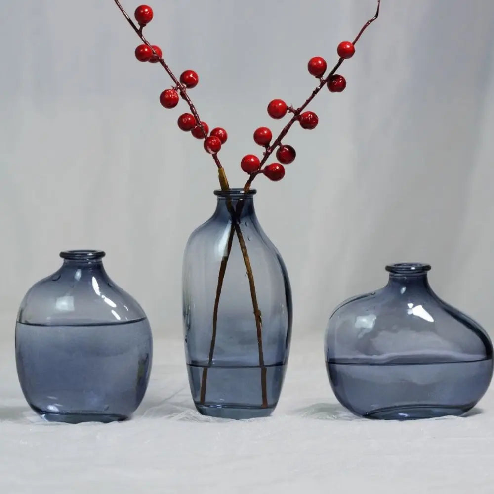 Set of three blue glass vases with a branch and red berries on a light gray background. Boho Home Decor.
