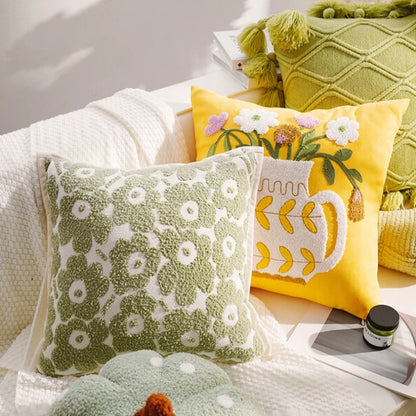 Decorative pillows on a sofa with a yellow floral pillow, green patterned pillow, and white pillow with a cup design.