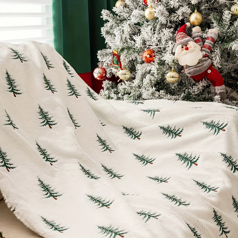 White blanket with green tree patterns in front of a decorated Christmas tree.