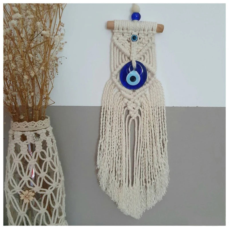 Macrame wall hanging with a blue evil eye charm on a plain background