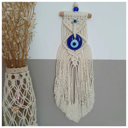 Macrame wall hanging with a blue evil eye charm on a plain background