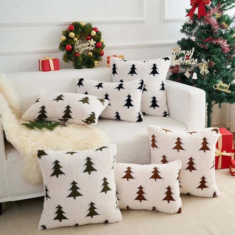 White sofa with Christmas tree-patterned cushions, decorated Christmas tree, and wreath in the background.