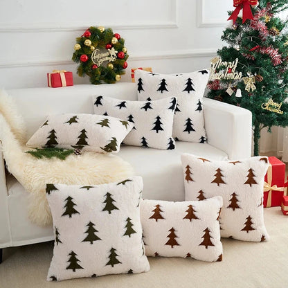 White sofa with Christmas tree-patterned cushions, decorated Christmas tree, and wreath in the background.