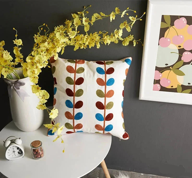 Decorative pillow with colorful leaf pattern on a table with flowers and a clock.floral embroidery on linen cotton cushion cover – boho home decor accent