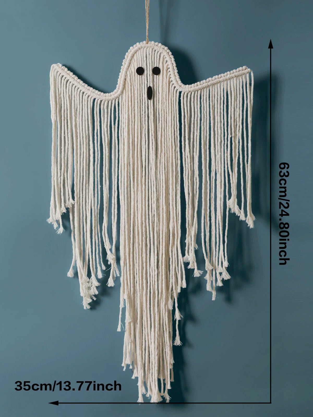 A ghost-shaped macrame wall hanging made from off-white cotton cord, shown against a muted blue-gray background with black dimension arrows and text indicating 63cm height and 35cm width from My Boho Home