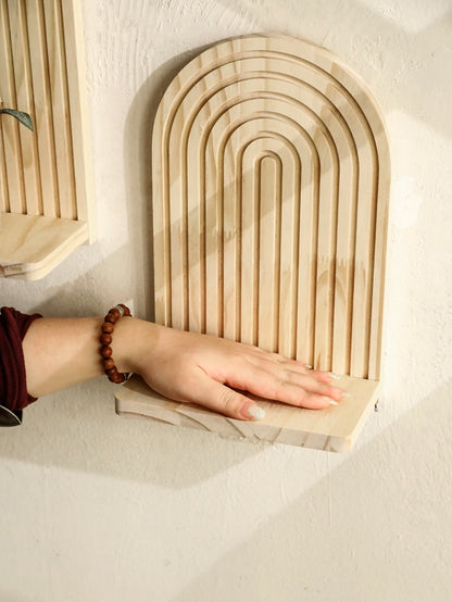 Wooden arch-shaped shelves on a white wall with a hand reaching out to touch one of them.