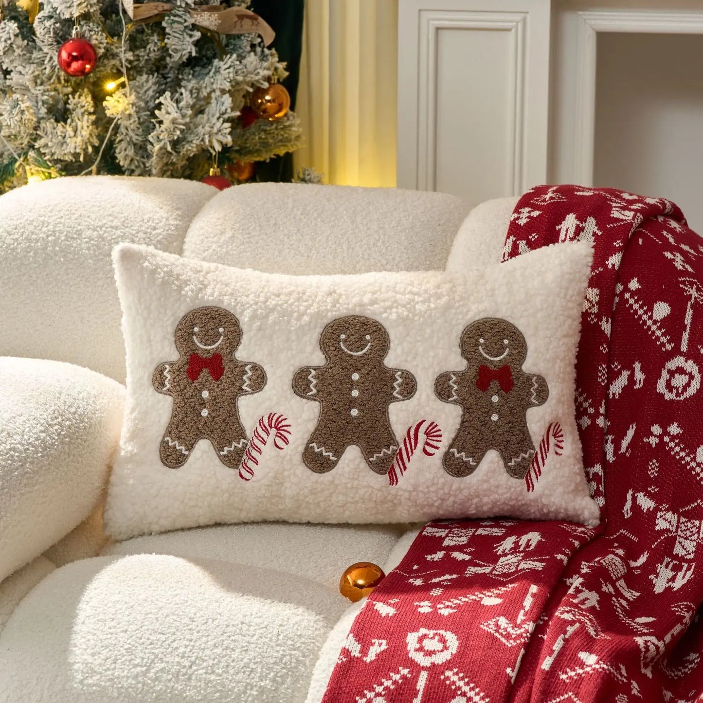 Decorative pillow with gingerbread men design on a white couch with a red patterned blanket.
