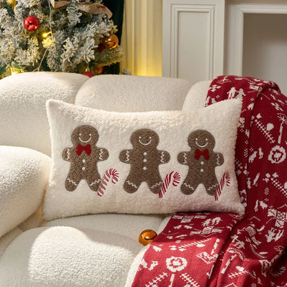 Decorative pillow with gingerbread men design on a white couch with a red patterned blanket.
