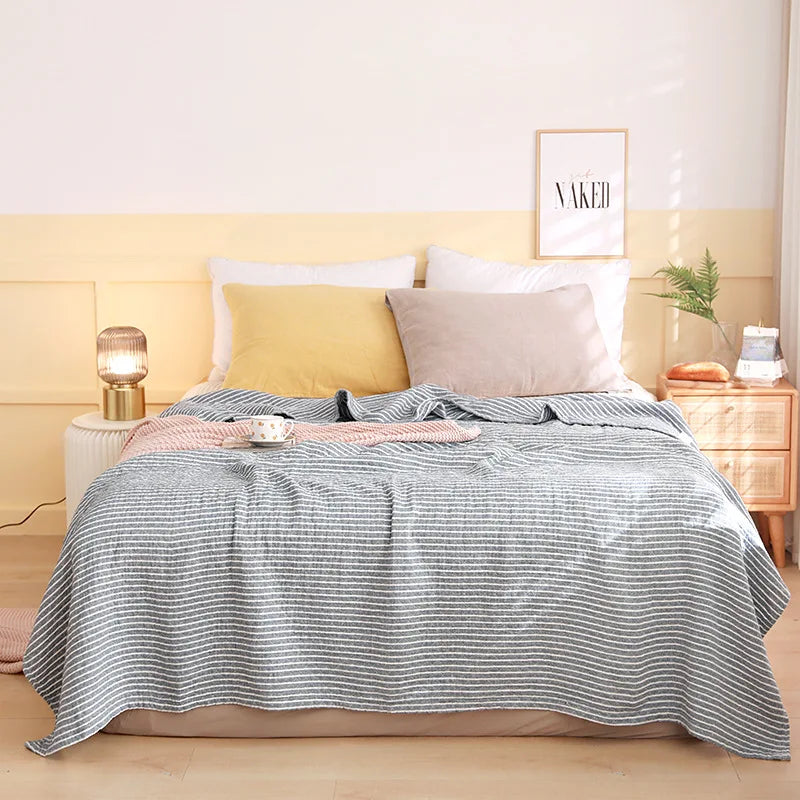 Bed with striped blanket and pillows in a bedroom setting. Boho Lightweight microfiber summer blanket for bed or sofa, cooling breathable throw for home, dorm, or office naps with geometric jacquard pattern.